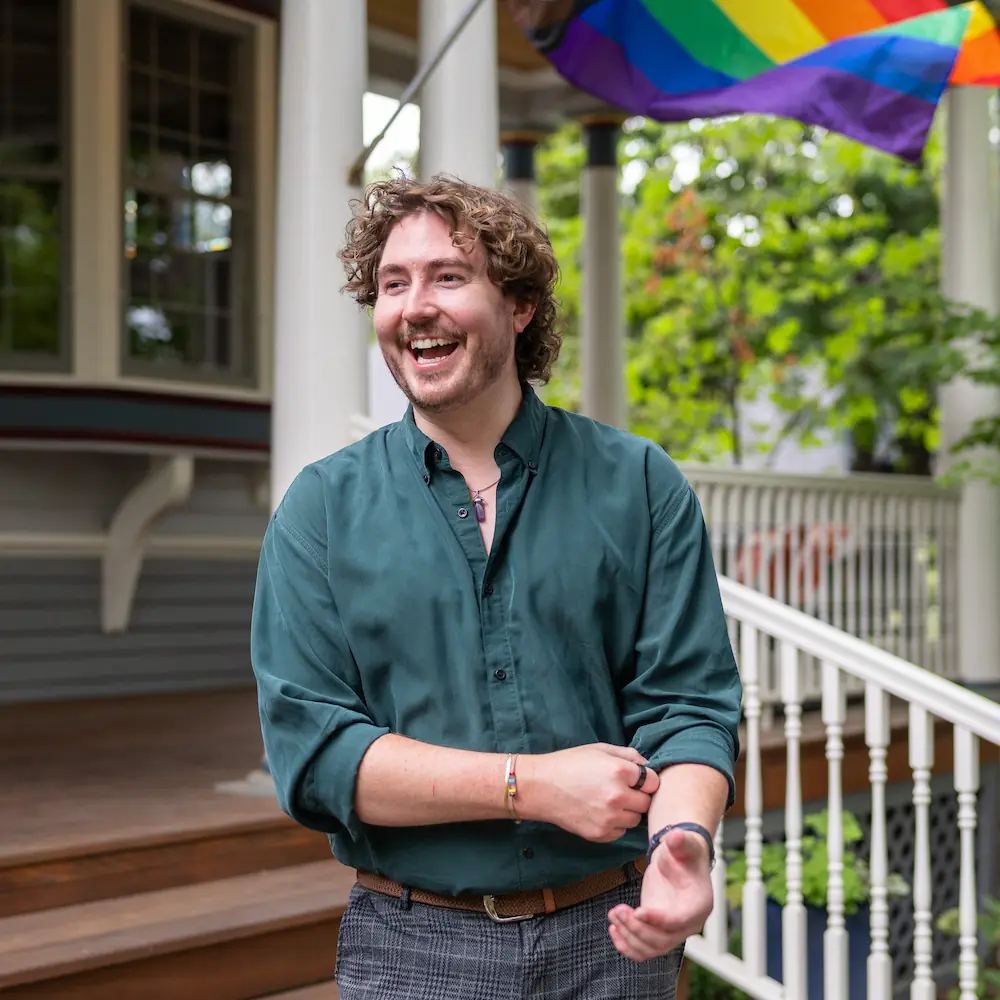 Joshua Barkes laughing in the North End in front of pride flag