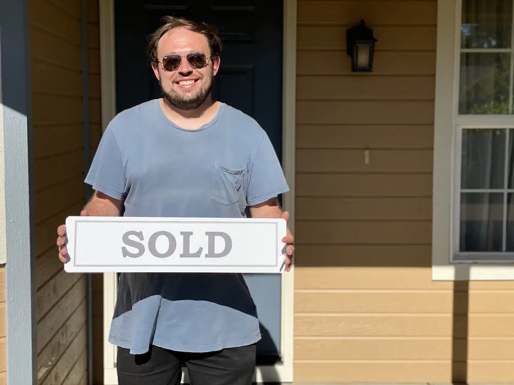 Happy first-time Buyer client holding a sold sign in front of his single-level home in Meridian, ID.